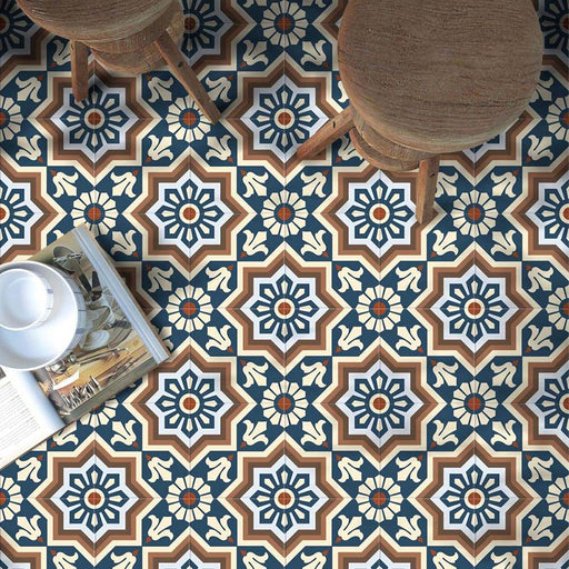 Brompton Grand 20x20cm Victorian-Moroccan-style ceramic floor tiles in a marketing setting, featuring intricate star and floral patterns in navy blue, white, and terracotta tones, styled with wooden stools and an open magazine on the floor.