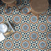 Brompton Grand 20x20cm Victorian-Moroccan-style ceramic floor tiles in a marketing setting, featuring intricate star and floral patterns in navy blue, white, and terracotta tones, styled with wooden stools and an open magazine on the floor.
