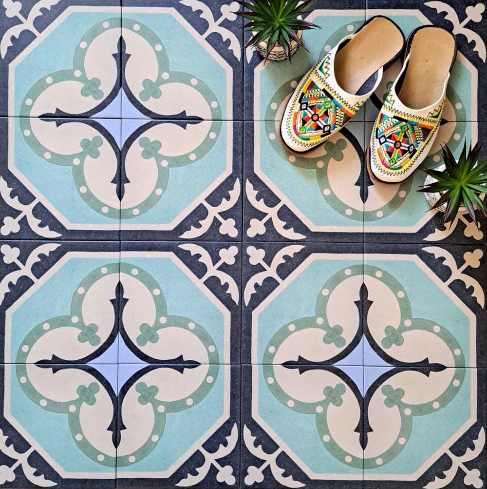 Overhead view of Europa Gothenberg 20x20cm Victorian Moroccan style floor tiles in blue, mint green and cream tones, forming a geometric pattern, styled with decorative shoes and small plants.