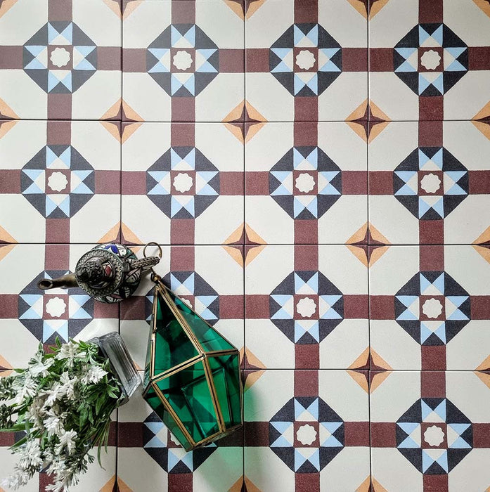 Overhead view of Europa Berlin 20x20cm Victorian Moroccan style floor tiles in burgundy, blue, mustard and cream tones, forming a geometric repeating pattern, styled with decorative lantern and floral arrangement.