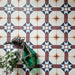Overhead view of Europa Berlin 20x20cm Victorian Moroccan style floor tiles in burgundy, blue, mustard and cream tones, forming a geometric repeating pattern, styled with decorative lantern and floral arrangement.