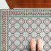 Empire Green 15x15cm Victorian floor tiles with matching border, featuring an ornate floral and geometric pattern in sage green, terracotta, and white tones, styled in a hallway setting with wooden door and pink shoes for scale.
