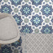 Brompton Royal Victorian Pattern 20x20cm ceramic tiles used in a styled interior setting, showing a repeating geometric star and floral design in blue, teal, and grey tones beneath a grey chair and patterned rug.