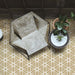 Maroush Mareshan Vintage Gold 18.7x21.6cm Moroccan hexagonal tiles with intricate white star patterns, styled in a modern interior with a concrete chair, potted plants, and warm golden tones for an artisan-inspired look.