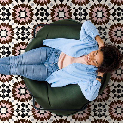 Cabana Mexico City Rose Moroccan Style 20x20cm tiles shown in a marketing setting with a person relaxing on a green chair. The floor features a geometric star pattern in rose pink, brown, black, and white with a smooth matt finish