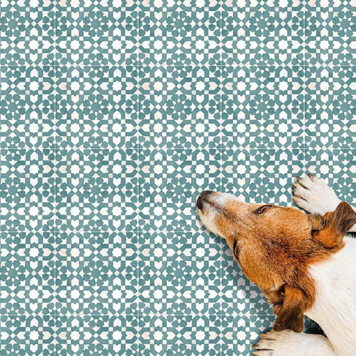 Bedouin Tetuan Green Moroccan-style 15x15cm tiles shown in a lifestyle setting with a dog resting on the patterned surface, featuring intricate geometric star and cross motifs in soft green and off-white tones with a handcrafted matte finish.