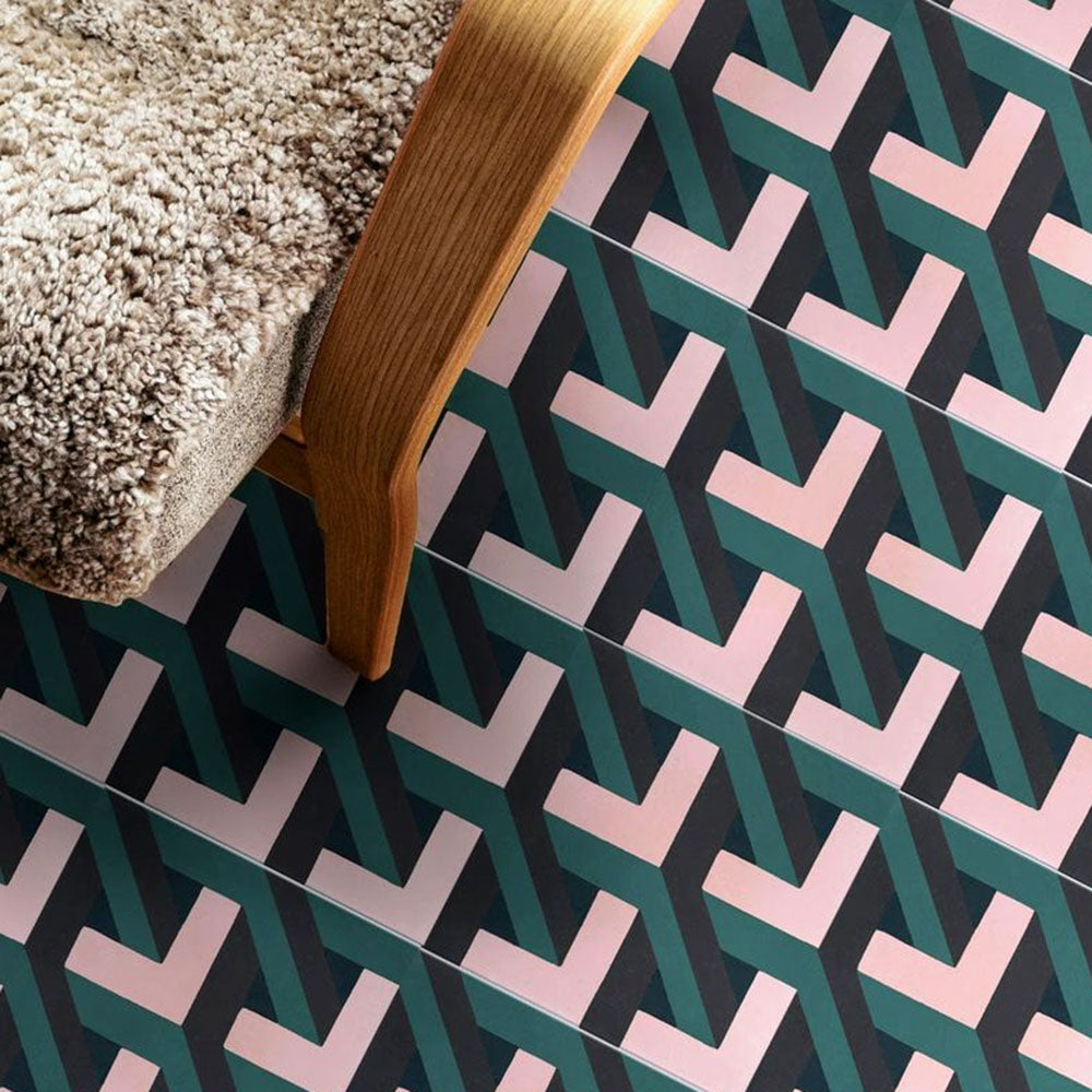 Living room setting featuring Geometry Lagoon 20x20cm patterned ceramic floor tiles, showcasing an interlocking geometric design in teal, blush pink, and charcoal tones, styled with a wooden chair and textured cushion.