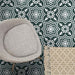 Brompton Victorian Green 20x20cm geometric patterned ceramic tiles in a marketing setting, featuring a white star and floral design on a deep green background, styled with a grey upholstered chair and beige patterned rug.