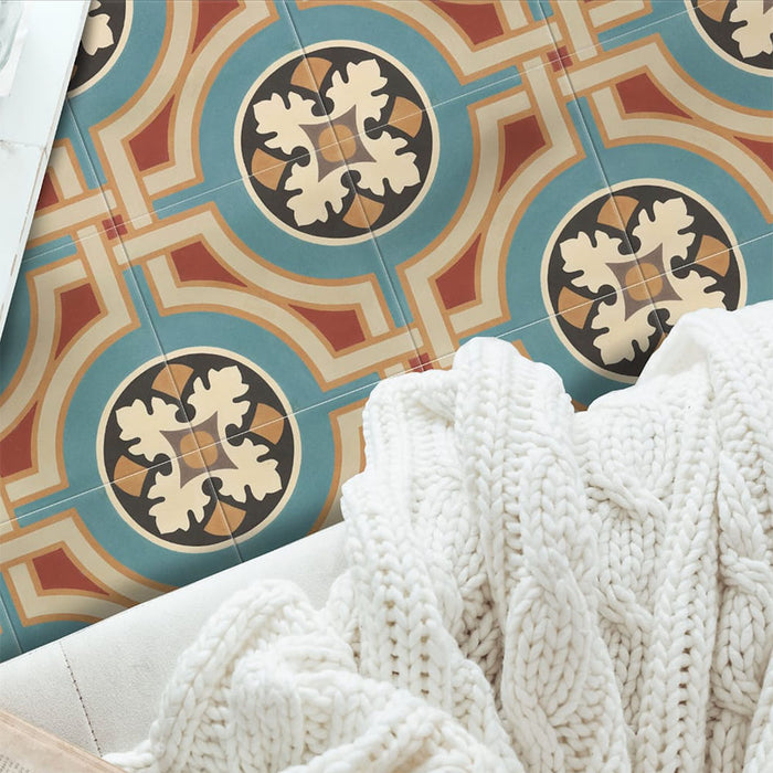Overhead view of Europa Helsinki 20x20cm Victorian Moroccan style floor tiles in teal, terracotta, cream and black tones, forming a decorative geometric pattern, styled with a soft knitted blanket in a cosy interior setting.