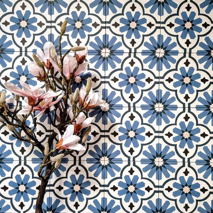 Flatlay featuring Clarence House Azul Blue 20x20cm Victorian Moroccan-style porcelain tiles, styled with pink magnolia flowers to highlight the intricate blue and white geometric pattern.