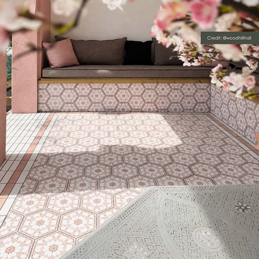 Outdoor seating area featuring Maroush Dusty Pink 18.7cm x 21.6cm Moroccan style hexagon tiles across the floor and built-in seating, showcasing an intricate pink and white geometric pattern with coordinating border tiles.