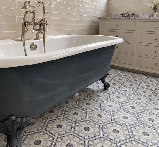 Bathroom featuring Maroush Frost Blue 18.7x21.6cm Moroccan-style hexagon floor tiles, with intricate blue, grey and white floral patterns, paired with a freestanding navy clawfoot bath, neutral brick wall tiles and traditional chrome fittings.