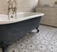 Bathroom featuring Maroush Frost Blue 18.7x21.6cm Moroccan-style hexagon floor tiles, with intricate blue, grey and white floral patterns, paired with a freestanding navy clawfoot bath, neutral brick wall tiles and traditional chrome fittings.