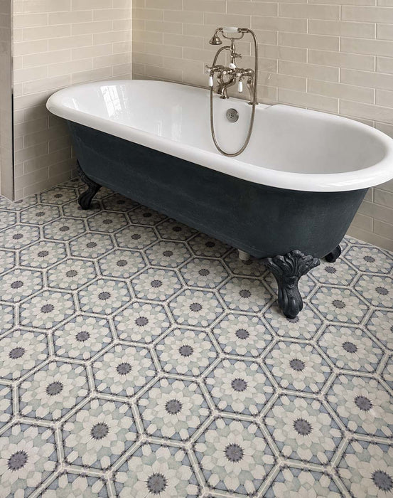 Bathroom featuring Maroush Frost Blue 18.7x21.6cm Moroccan-style hexagon floor tiles, with intricate blue, grey and white floral patterns, paired with a freestanding navy clawfoot bath, neutral brick wall tiles and traditional chrome fittings.