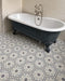 Bathroom featuring Maroush Frost Blue 18.7x21.6cm Moroccan-style hexagon floor tiles, with intricate blue, grey and white floral patterns, paired with a freestanding navy clawfoot bath, neutral brick wall tiles and traditional chrome fittings.