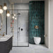 Bathroom featuring Mizu Blue Fluted Decor 6cm x 24cm gloss porcelain tiles across a curved feature wall, showcasing a rich blue-green finish and textured fluted surface, paired with soft blue patterned tiles and black shower fixtures.