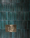 Close-up of Mizu Blue Fluted Decor 6cm x 24cm gloss porcelain tiles, showcasing a rich blue-green finish, tonal variation and textured fluted surface, paired with a brushed brass flush plate.