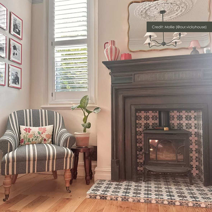Living room fireplace featuring Mamounia River Blue 20x20cm Moroccan-style ceramic wall and floor tiles, styled with a cast iron stove, dark timber surround, striped armchair, and warm wood flooring.