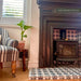 Living room interior featuring Mamounia River Blue 20x20cm Moroccan-style ceramic wall and floor tiles, paired with a cast iron stove, traditional fireplace, striped armchair, wall art, and soft neutral décor.