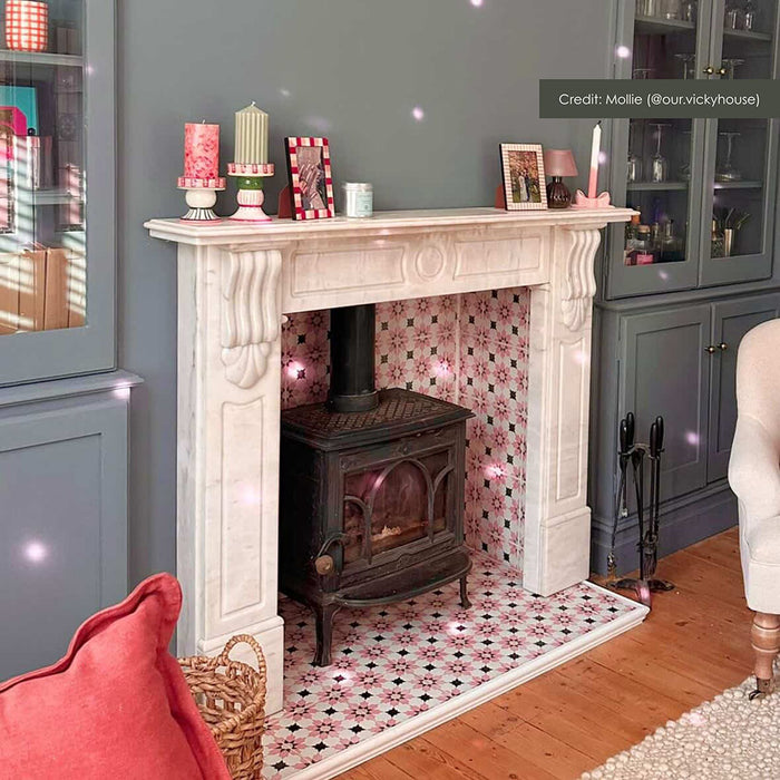 Living room fireplace featuring Mamounia Rose 20x20cm Moroccan-style ceramic wall and floor tiles, styled with a cast iron stove, marble surround, soft grey cabinetry, and warm wood flooring.