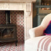 Fireplace detail featuring Mamounia Rose 20x20cm Moroccan-style ceramic wall and floor tiles, paired with a cast iron stove, carved marble surround, and soft furnishings with pink accents.