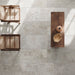 Monastry Flagstone XL Grey Tumbled Travertine 50 × 100cm porcelain floor tiles, styled with warm wood furniture and woven textures to highlight soft tonal variation, a gently aged finish, and a relaxed, natural stone effect.