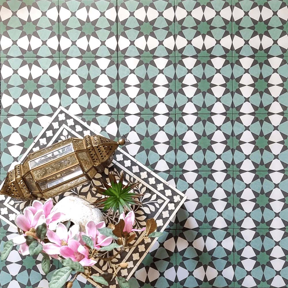 Moroccan-inspired interior featuring Agraba Verde 20x20cm patterned tiles with green, turquoise, and white geometric star motifs, styled with a brass lantern, floral decor, and an intricately patterned side table for an authentic artisan look.