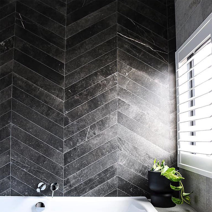 Bathroom featuring Obsidian Stone Chevron Nite 10x53cm stone-effect porcelain wall tiles in a chevron layout, styled in deep charcoal tones with a modern bath, chrome fixtures and minimalist contemporary décor.