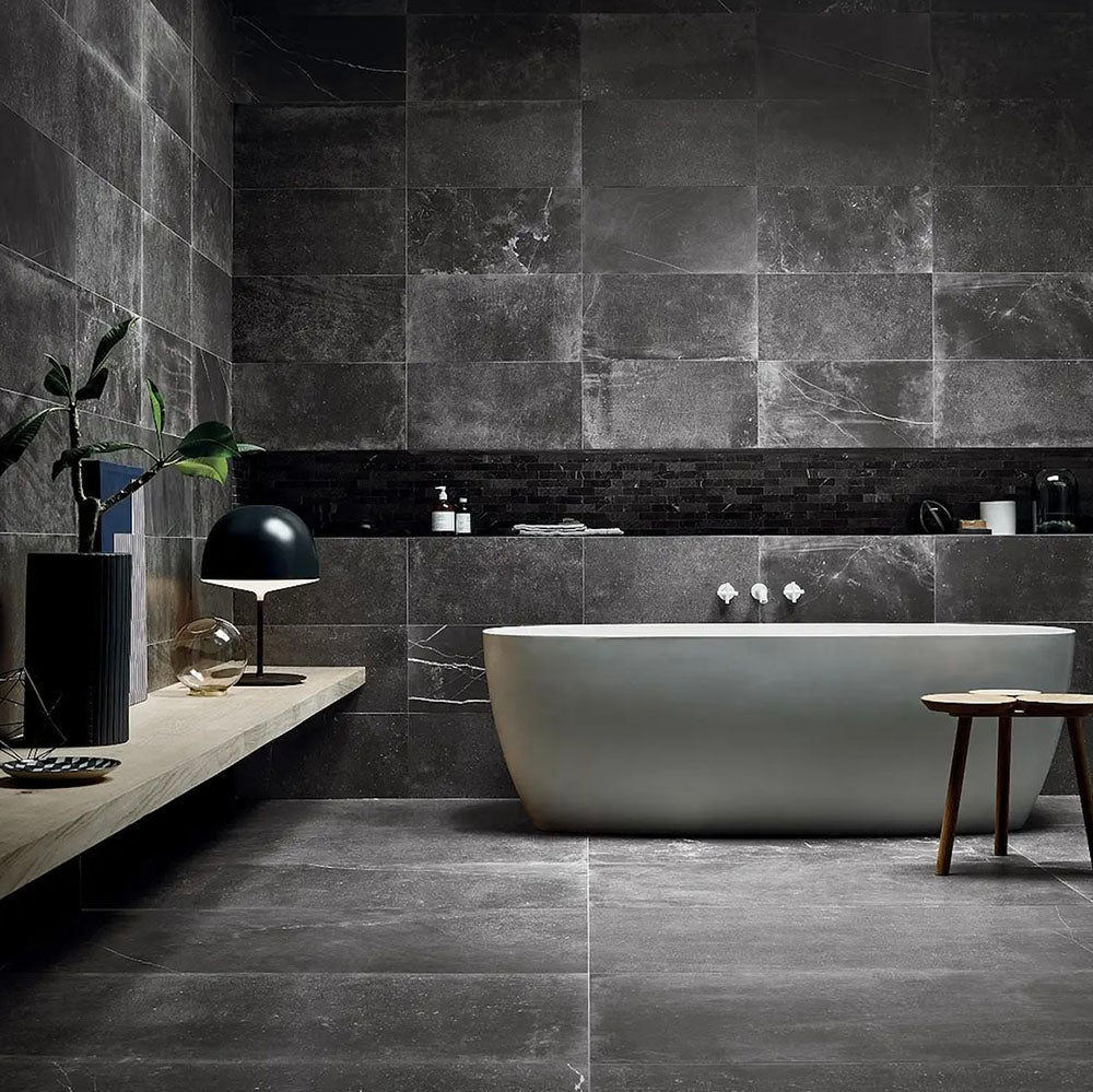 Modern bathroom featuring Obsidian Stone Nite 30x60cm stone-effect porcelain wall and floor tiles in deep charcoal tones, styled with a freestanding bath, black accents, textured mosaics and minimalist contemporary décor.