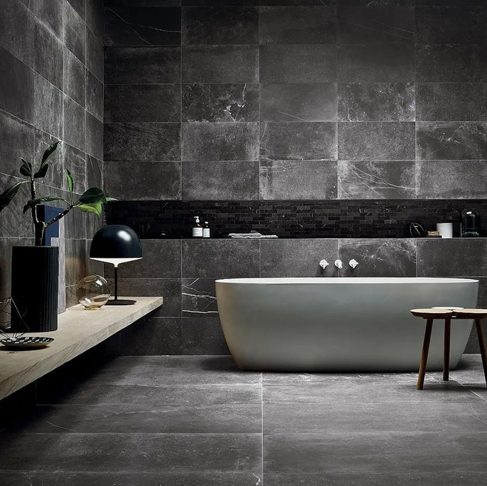 Modern bathroom featuring Obsidian Stone Nite 30x60cm stone-effect porcelain wall and floor tiles in deep charcoal tones, styled with a freestanding bath, black accents, textured mosaics and minimalist contemporary décor.