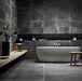 Modern bathroom featuring Obsidian Stone Nite 30x60cm stone-effect porcelain wall and floor tiles in deep charcoal tones, styled with a freestanding bath, black accents, textured mosaics and minimalist contemporary décor.
