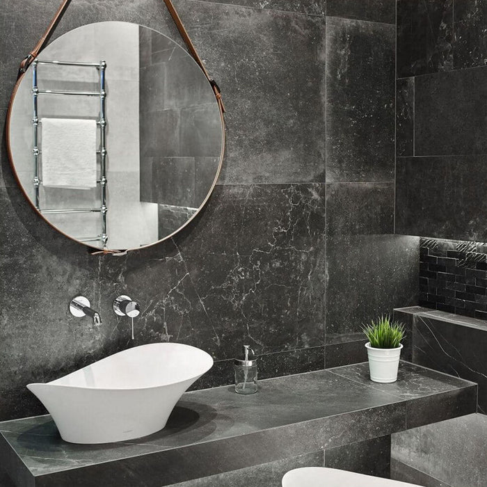 Contemporary bathroom featuring Obsidian Stone Nite 60x60cm stone-effect porcelain wall and floor tiles in dark charcoal tones, styled with a floating vanity, round leather mirror, black mosaic details and modern spa-inspired décor.