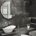 Contemporary bathroom featuring Obsidian Stone Nite 60x60cm stone-effect porcelain wall and floor tiles in dark charcoal tones, styled with a floating vanity, round leather mirror, black mosaic details and modern spa-inspired décor.