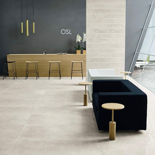 Contemporary commercial interior featuring Obsidian Stone Sand 60x60cm stone-effect porcelain floor tiles in soft beige tones, styled with minimalist furniture, warm wood finishes, black accents and large architectural glazing.