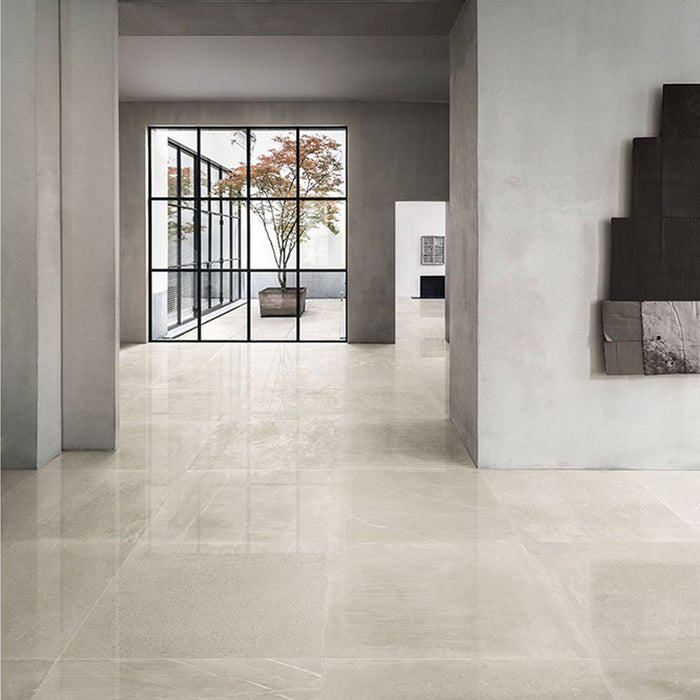 Modern interior featuring Obsidian Stone Sand 60x60cm stone-effect porcelain floor tiles in soft beige tones, styled with minimalist architecture, large black-framed glazing and contemporary neutral interiors filled with natural light.