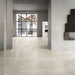 Modern interior featuring Obsidian Stone Sand 60x60cm stone-effect porcelain floor tiles in soft beige tones, styled with minimalist architecture, large black-framed glazing and contemporary neutral interiors filled with natural light.