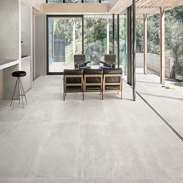 Living room featuring Obsidian Stone Silver 30x60cm stone-effect porcelain floor tiles in soft silver-grey tones, styled with modern leather seating, large glazing and contemporary open-plan interiors filled with natural light.