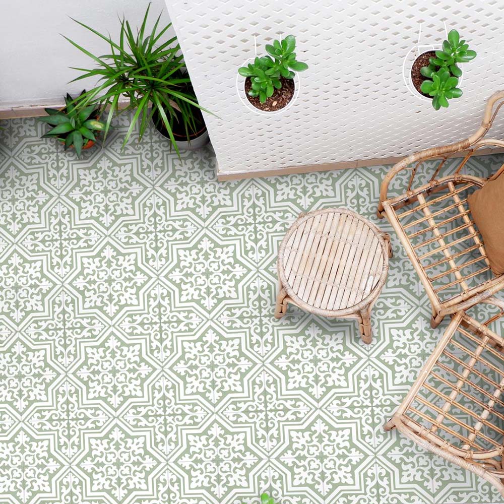 Overhead view of Europa Trondheim Sage Green 20x20cm Victorian Moroccan style floor tiles in sage green and cream tones, forming an intricate geometric pattern, styled with rattan furniture and potted plants in a bright interior setting.