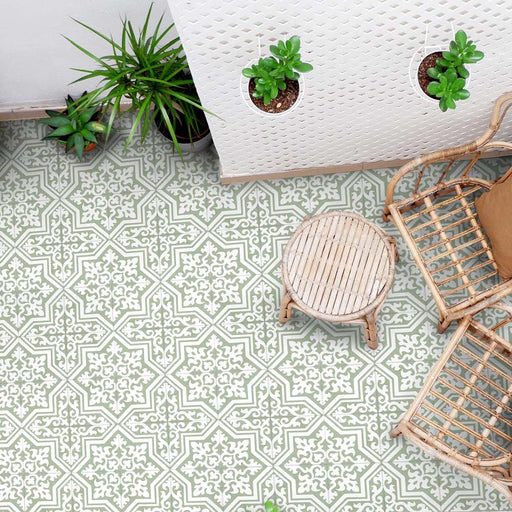 Overhead view of Europa Trondheim Sage Green 20x20cm Victorian Moroccan style floor tiles in sage green and cream tones, forming an intricate geometric pattern, styled with rattan furniture and potted plants in a bright interior setting.