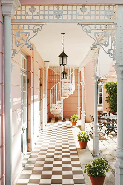 Outdoor courtyard featuring Maison Plain Black Base and Maison Plain White Base 20x20cm Victorian-style floor tiles, installed in a classic chequerboard layout, styled with decorative ironwork, soft pastel walls, and potted greenery.