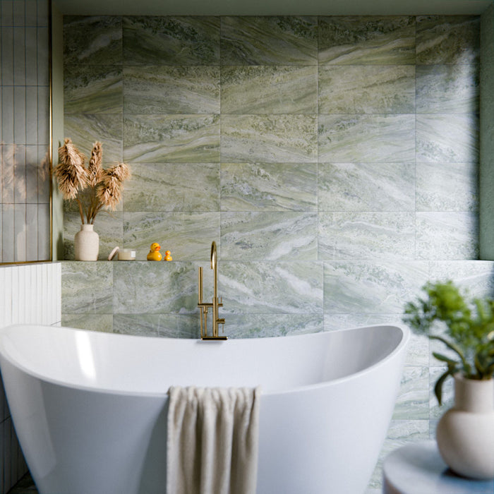 Bathroom featuring Paradis Marble Verde Green stone marble effect porcelain wall tiles in a 30cm x 60cm format, showcasing flowing green, sage and soft white veining inspired by natural marble, paired with a freestanding white bath, brushed brass brassware, neutral accessories and soft natural lighting for a luxurious spa-inspired interior.