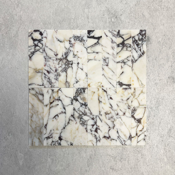 Grouped Fitzrovia Picasso 5 x 20cm honed natural marble tiles arranged together to showcase the overall variation of the range, featuring a light base with bold, expressive veining in deep charcoal, soft green, and warm golden tones, highlighting the natural character of the stone across multiple pieces.