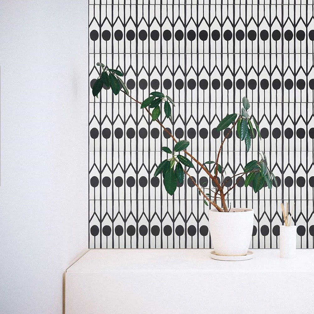 Alhambra Felisa 20x20cm Moroccan tiles used as a feature wall with a striking black and white linear pattern and circular motifs, styled with a green potted plant for a modern minimalist look.