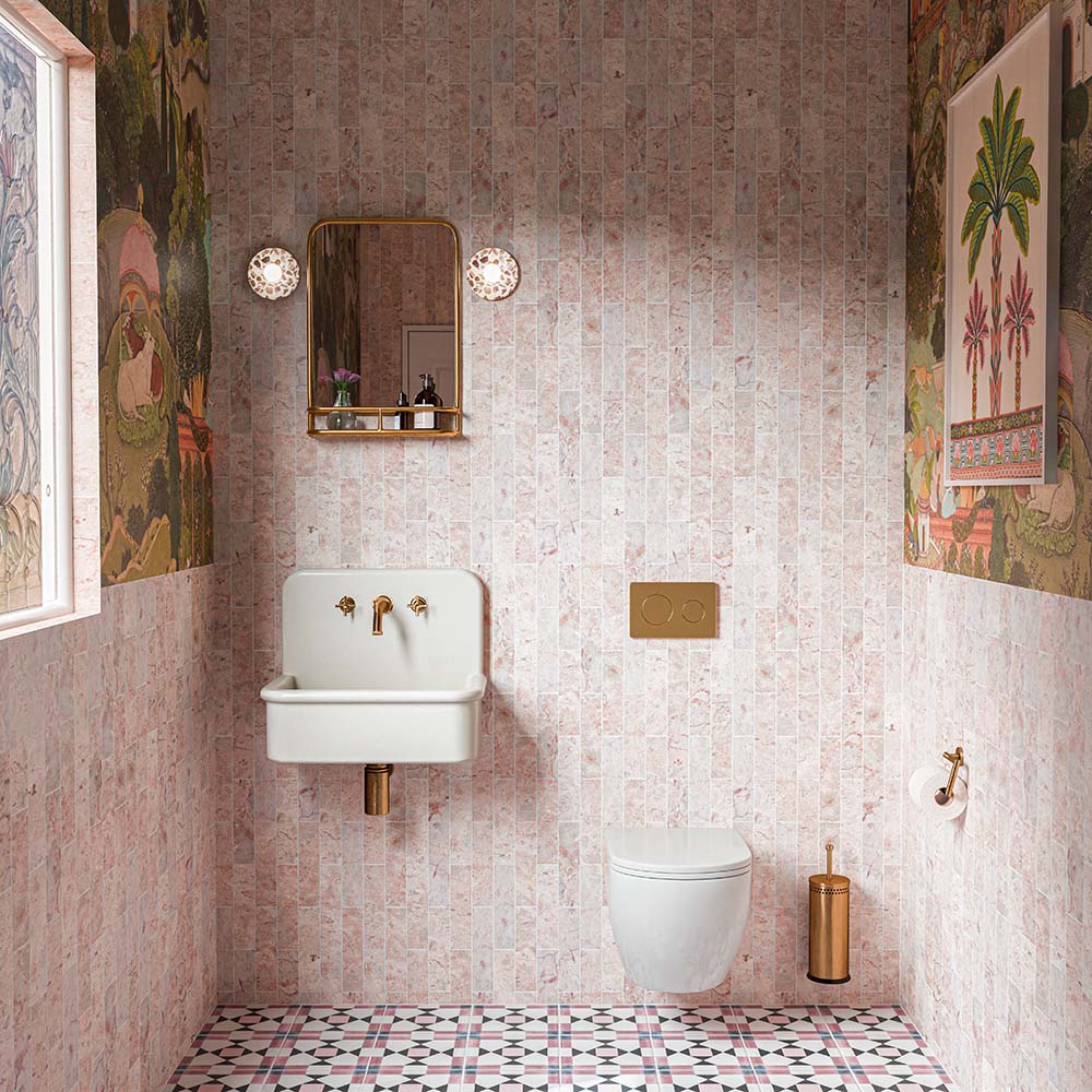 Bathroom featuring Ravine Rose 20x20cm Moroccan-style patterned tiles, with soft pink and rose tones arranged vertically on the walls, paired with decorative floor tiles, botanical wallpaper, a white wall-mounted basin and brass fittings.