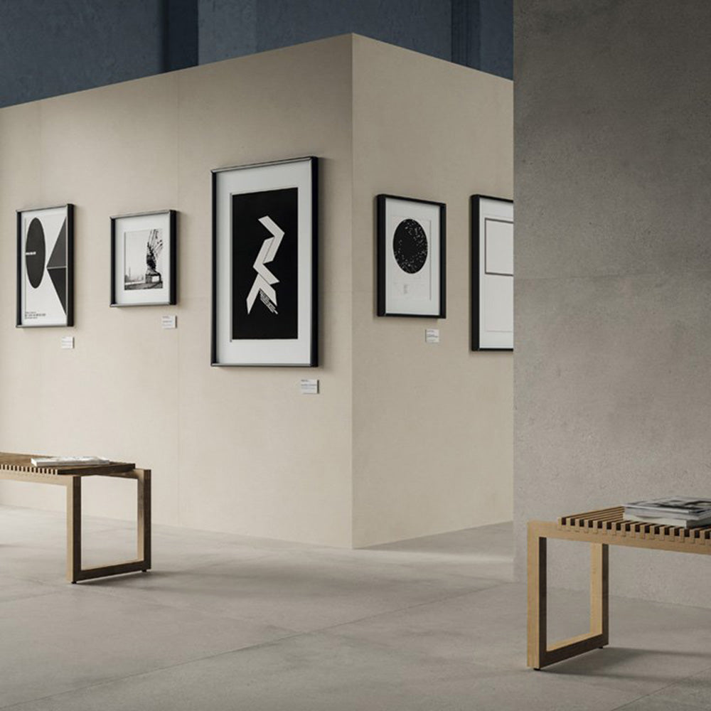 Contemporary gallery-style interior featuring Riminy Light concrete-style wall and floor tiles 60 × 60cm, showcasing soft light grey concrete-effect tones with subtle texture, paired with minimalist furnishings and modern monochrome artwork.
