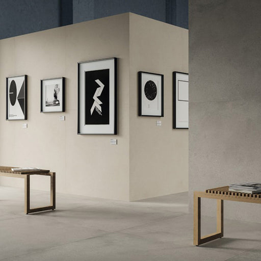 Contemporary gallery-style interior featuring Riminy Light concrete-style wall and floor tiles 60 × 60cm, showcasing soft light grey concrete-effect tones with subtle texture, paired with minimalist furnishings and modern monochrome artwork.
