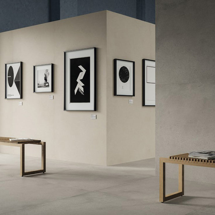 Contemporary gallery-style interior featuring Riminy Light concrete-style wall and floor tiles 60 × 60cm, showcasing soft light grey concrete-effect tones with subtle texture, paired with minimalist furnishings and modern monochrome artwork.