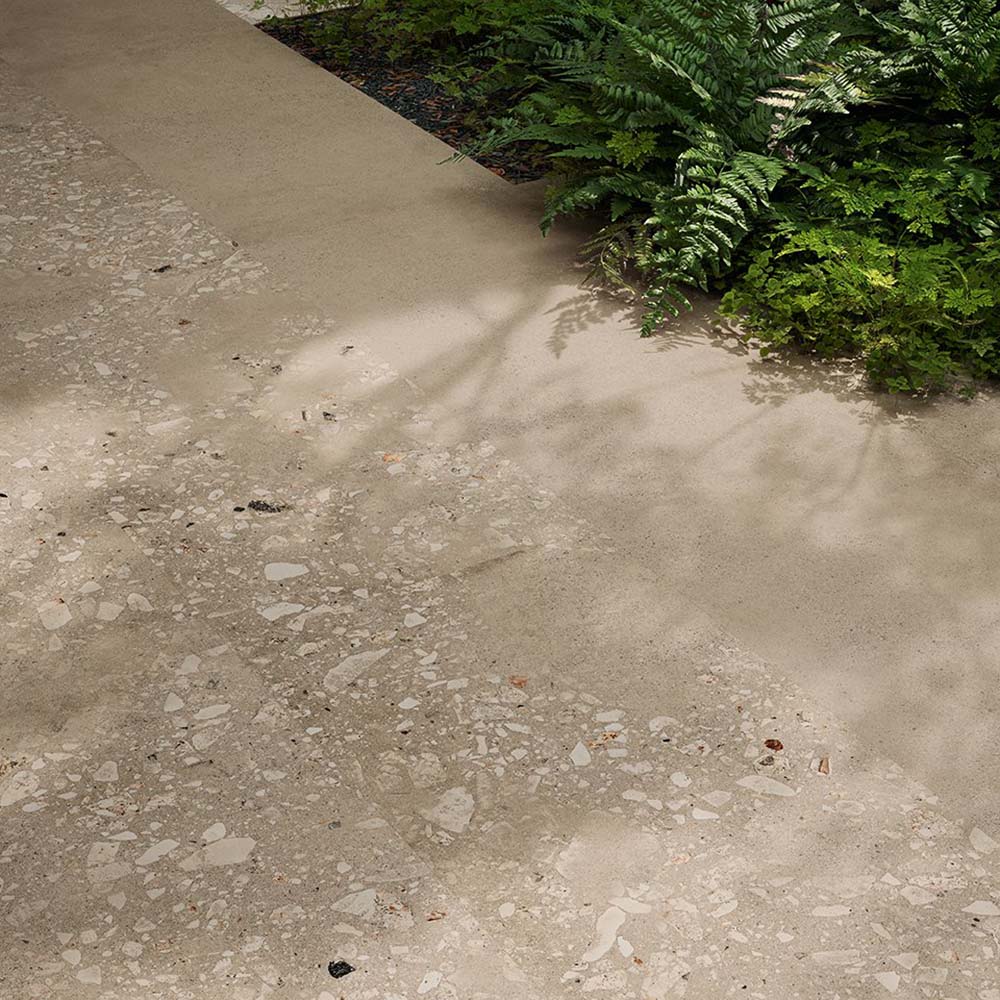 Outdoor garden pathway featuring Riminy Sand 20mm Thick Outdoor Cosmo Stone tile slabs 60 × 120cm, showcasing a warm terrazzo-effect surface with scattered stone fragments, soft sand-toned concrete detailing, and a durable contemporary finish paired with natural greenery.