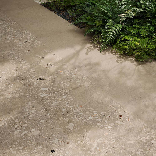 Outdoor garden pathway featuring Riminy Sand 20mm Thick Outdoor Cosmo Stone tile slabs 60 × 120cm, showcasing a warm terrazzo-effect surface with scattered stone fragments, soft sand-toned concrete detailing, and a durable contemporary finish paired with natural greenery.