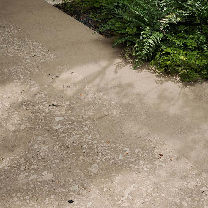 Outdoor garden pathway featuring Riminy Sand 20mm Thick Outdoor Cosmo Stone tile slabs 60 × 120cm, showcasing a warm terrazzo-effect surface with scattered stone fragments, soft sand-toned concrete detailing, and a durable contemporary finish paired with natural greenery.
